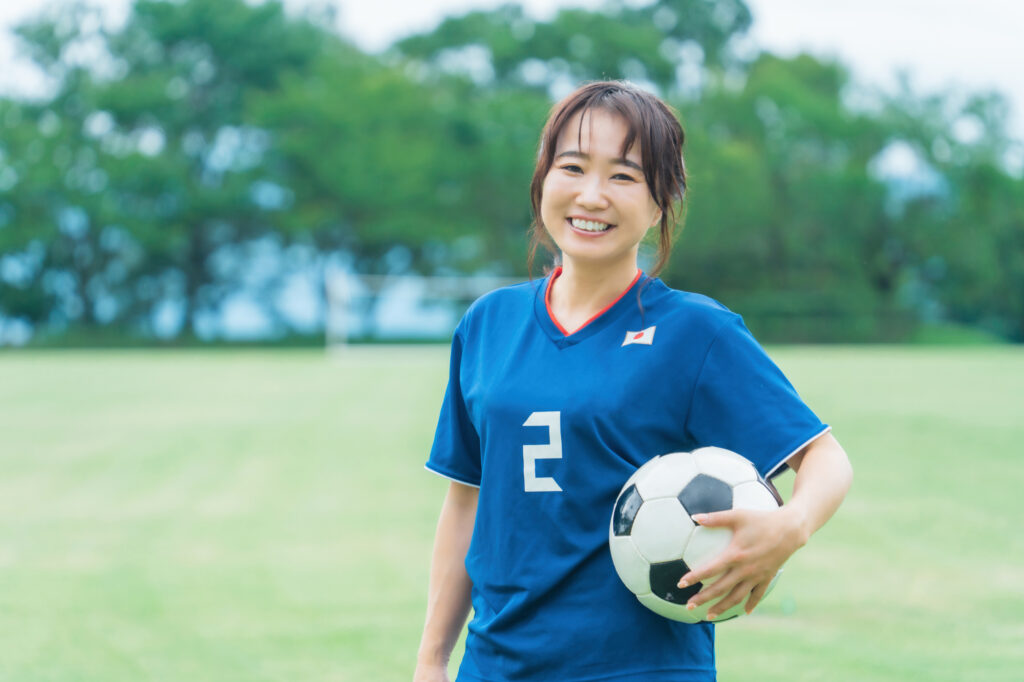 サッカーボールを持ちながら笑顔でサッカーするファン・サポーターの日本人女性